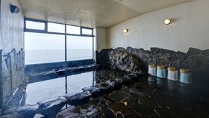 A stone-lined hot tub with a view of the sea, a window, and a stone wall. - Sakataya Ryokan (Yuza)