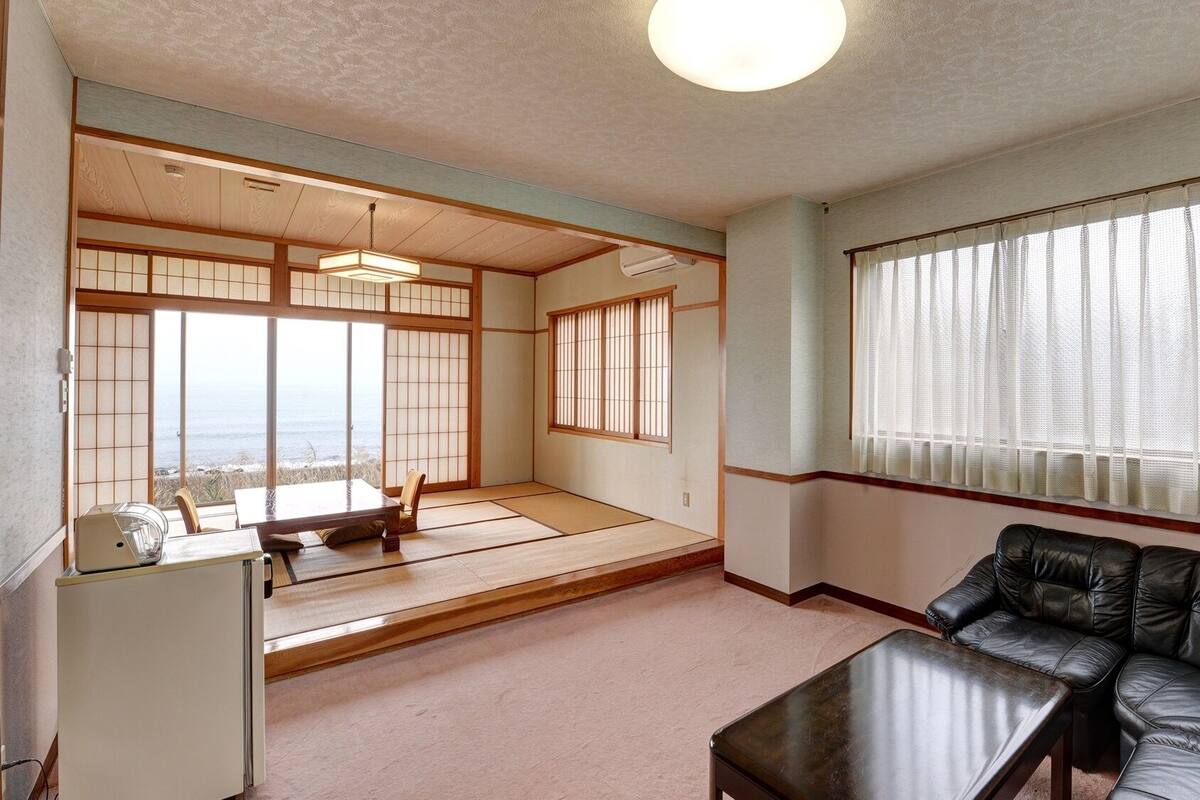 Una habitación japonesa tradicional con suelo de tatami, un espacio con esteras de tatami, un sofá de cuero negro, una mesita y vista al mar.