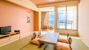 A room with tatami mats, a wooden table, a television, and a large window offering a view of the sea. - Ocean Front Hamada-kan (Hitachinaka)