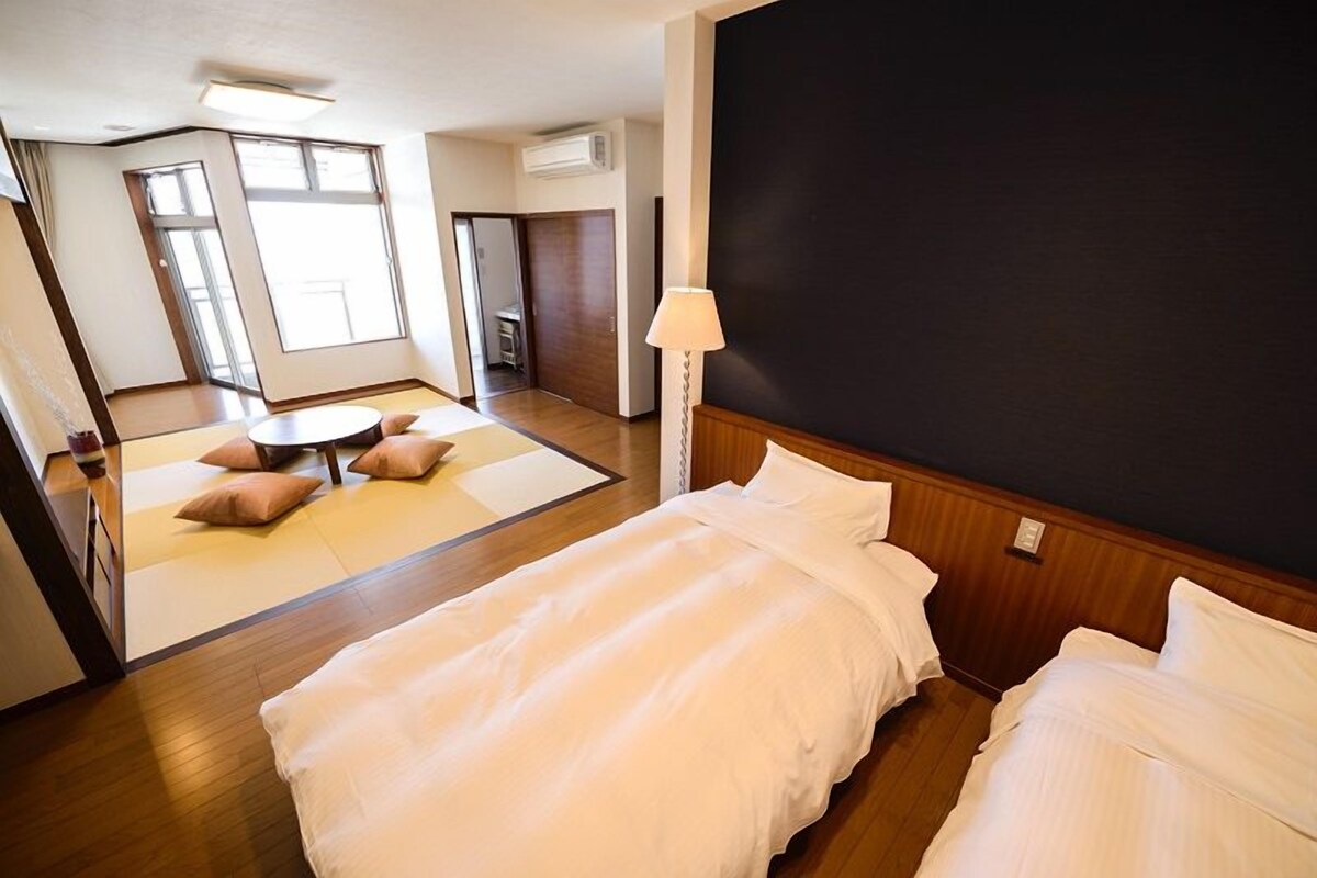 A hotel room with two beds, a large window, and a view of the outside.