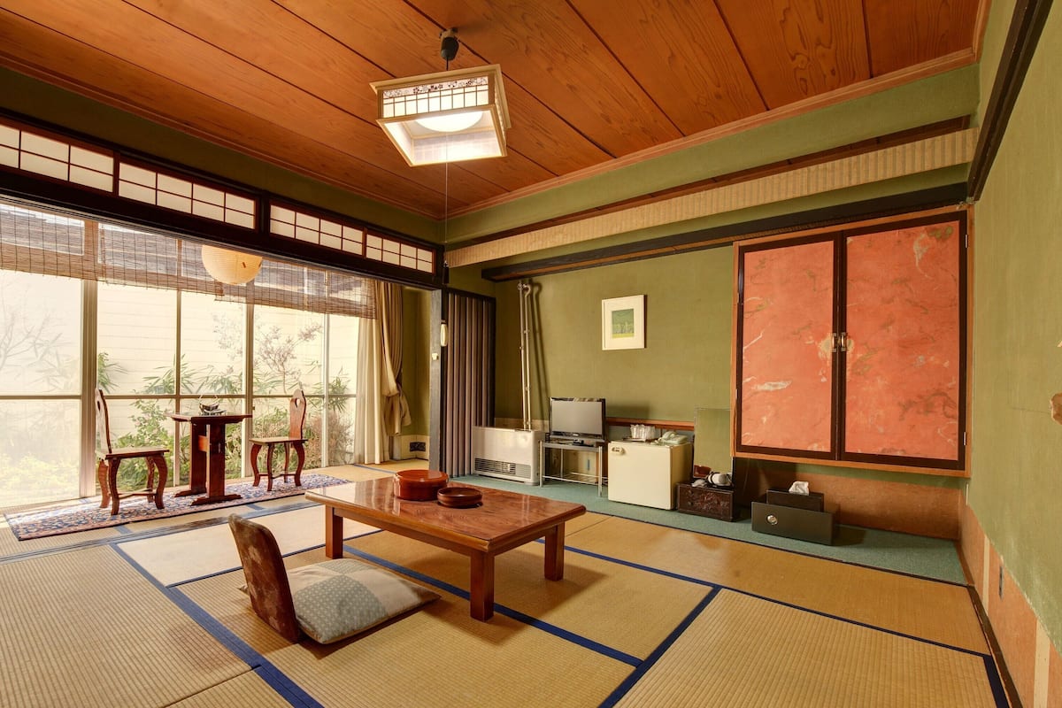 Una habitación tradicional japonesa con suelo de tatami, una mesa de madera, un televisor y una puerta corredera.