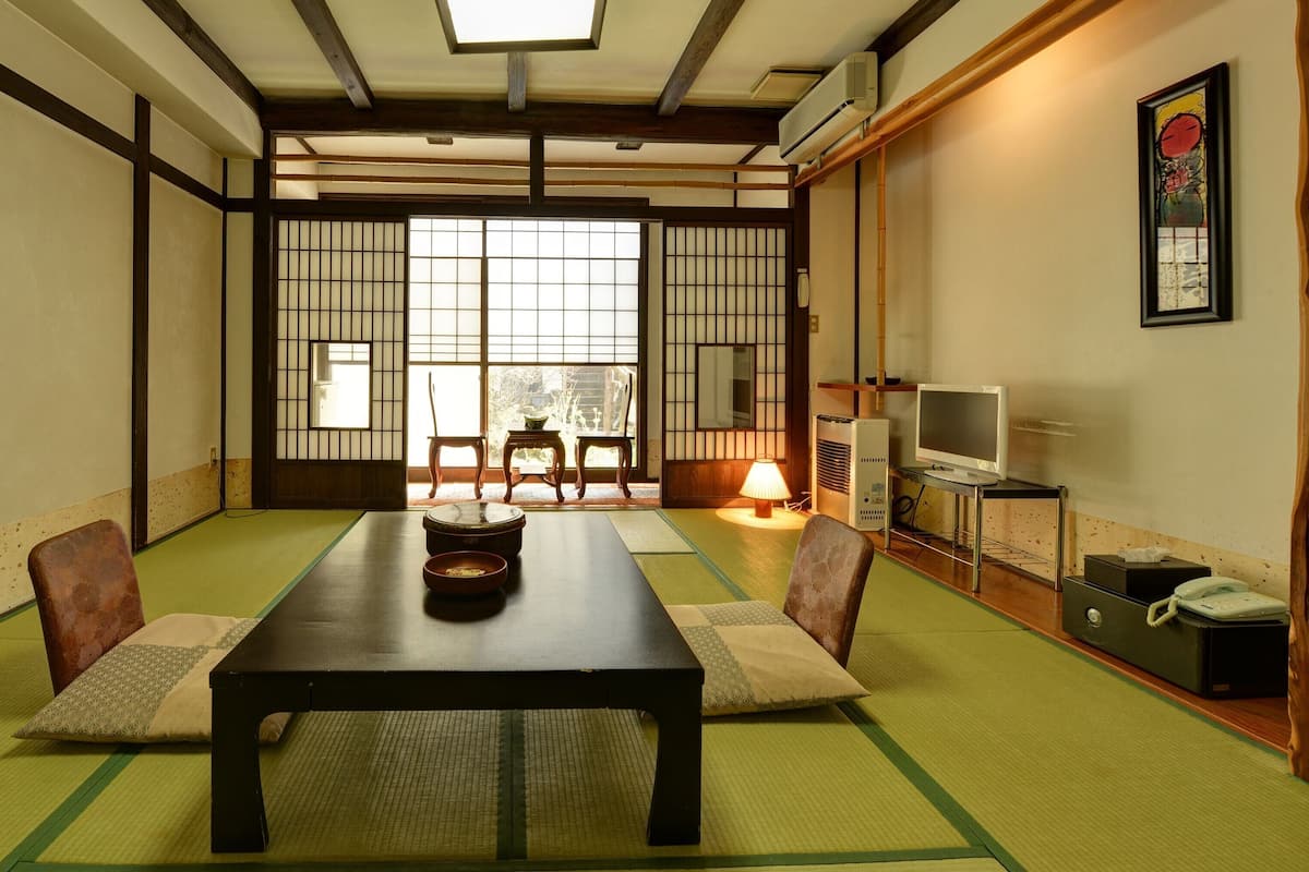 Una habitación japonesa tradicional con suelo de tatami, una mesa baja, dos sillas, un televisor y un calentador.