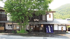 A traditional Japanese building with a signboard, a wooden entrance, and a view of a mountain.