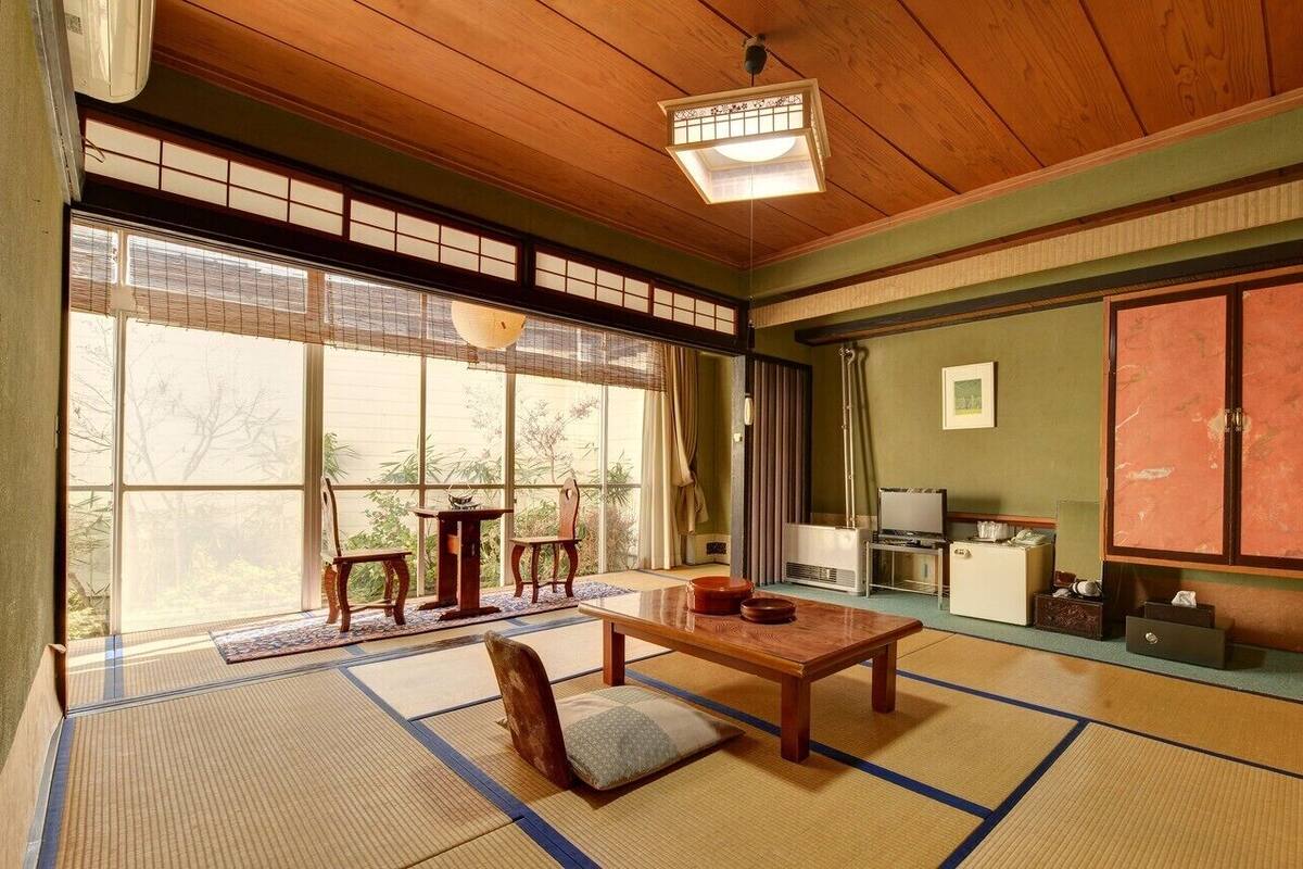 Una habitación tradicional japonesa con suelo de tatami, una mesa de madera baja, una silla acolchada, un televisor y una puerta corredera.