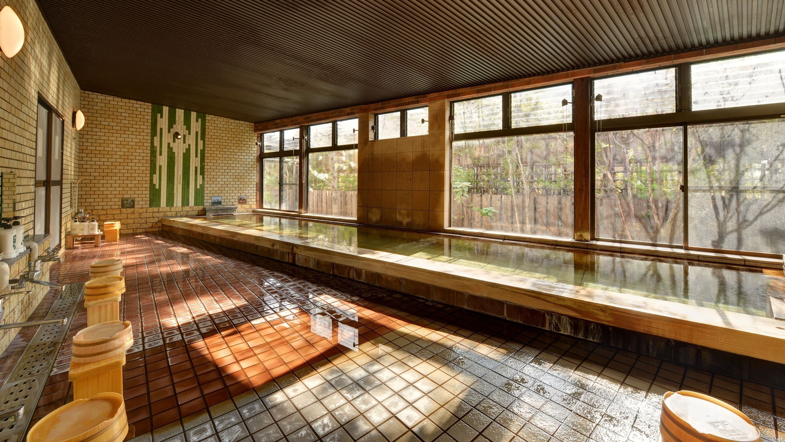 Une longue et étroite piscine dont le fond est carrelé et qui est bordée d’un côté de bancs en bois.