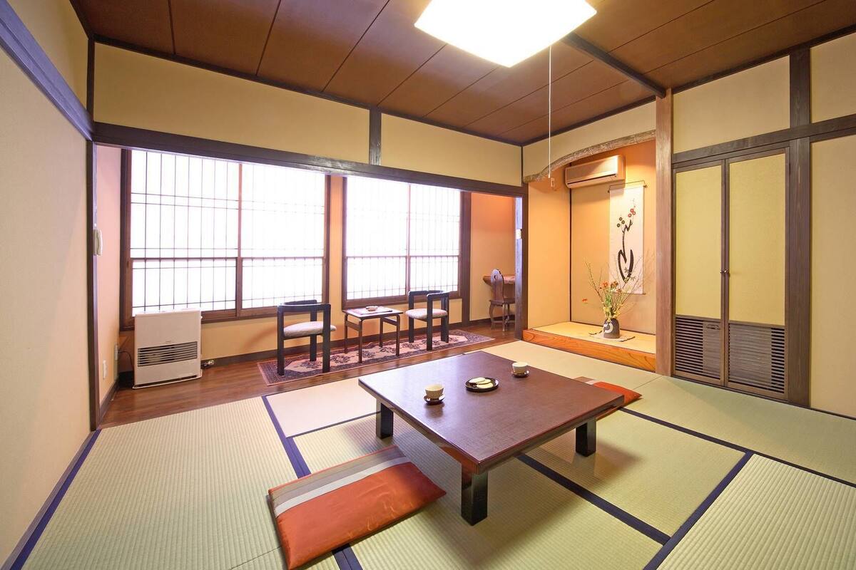 Una habitación tradicional japonesa con suelo de tatami, una mesa baja con cojines y puertas correderas.