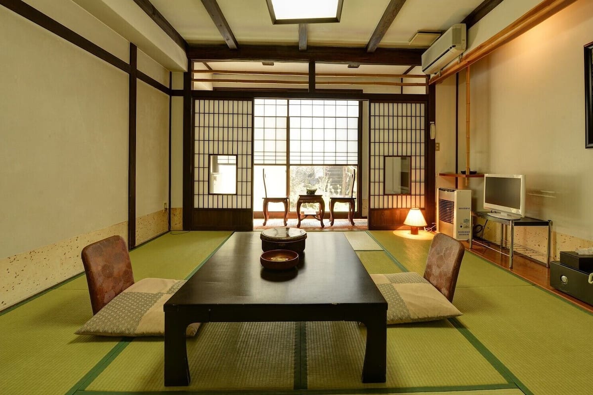 Una habitación japonesa tradicional con suelo de tatami, una mesa baja y puertas correderas.