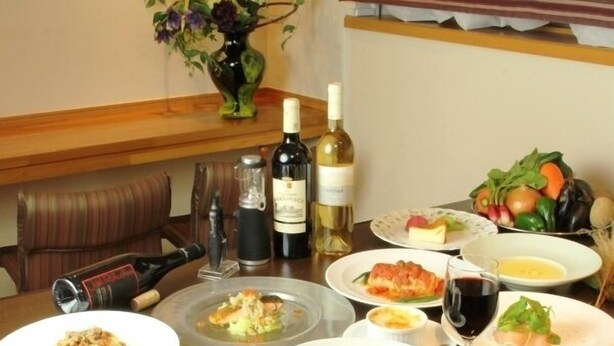 Una mesa de comedor con diversos platos, botellas de vino y un jarrón con flores.