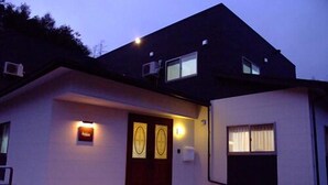 Una casa moderna de dos pisos, con techo oscuro, entrada frontal y un pequeño porche.
