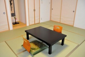 A tatami mat room with a low table and two chairs. - Fukuokaya Ryokan (Setouchi)