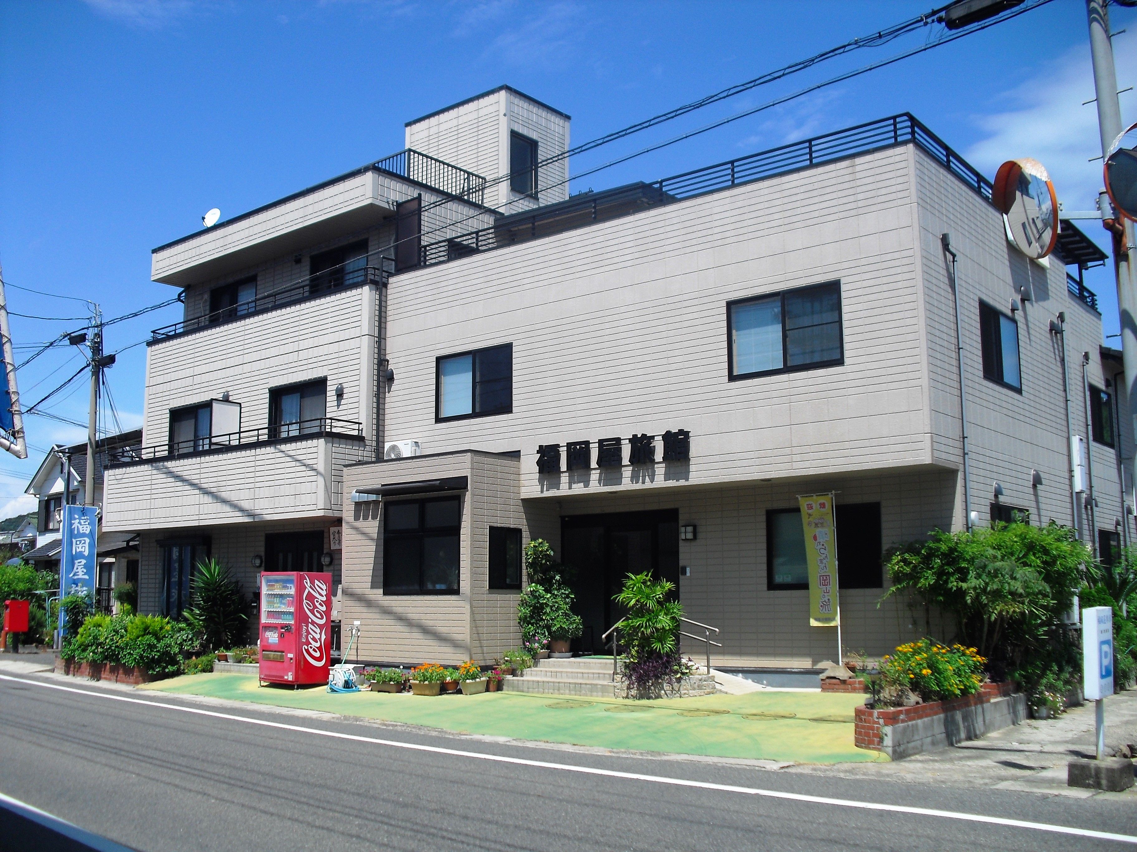 A two-story building with a flat roof, multiple windows, and a Coca-Cola vending machine on the ground floor.