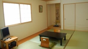 A room with tatami flooring, a low table, a television on a stand, and sliding doors. - Fukuokaya Ryokan (Setouchi)