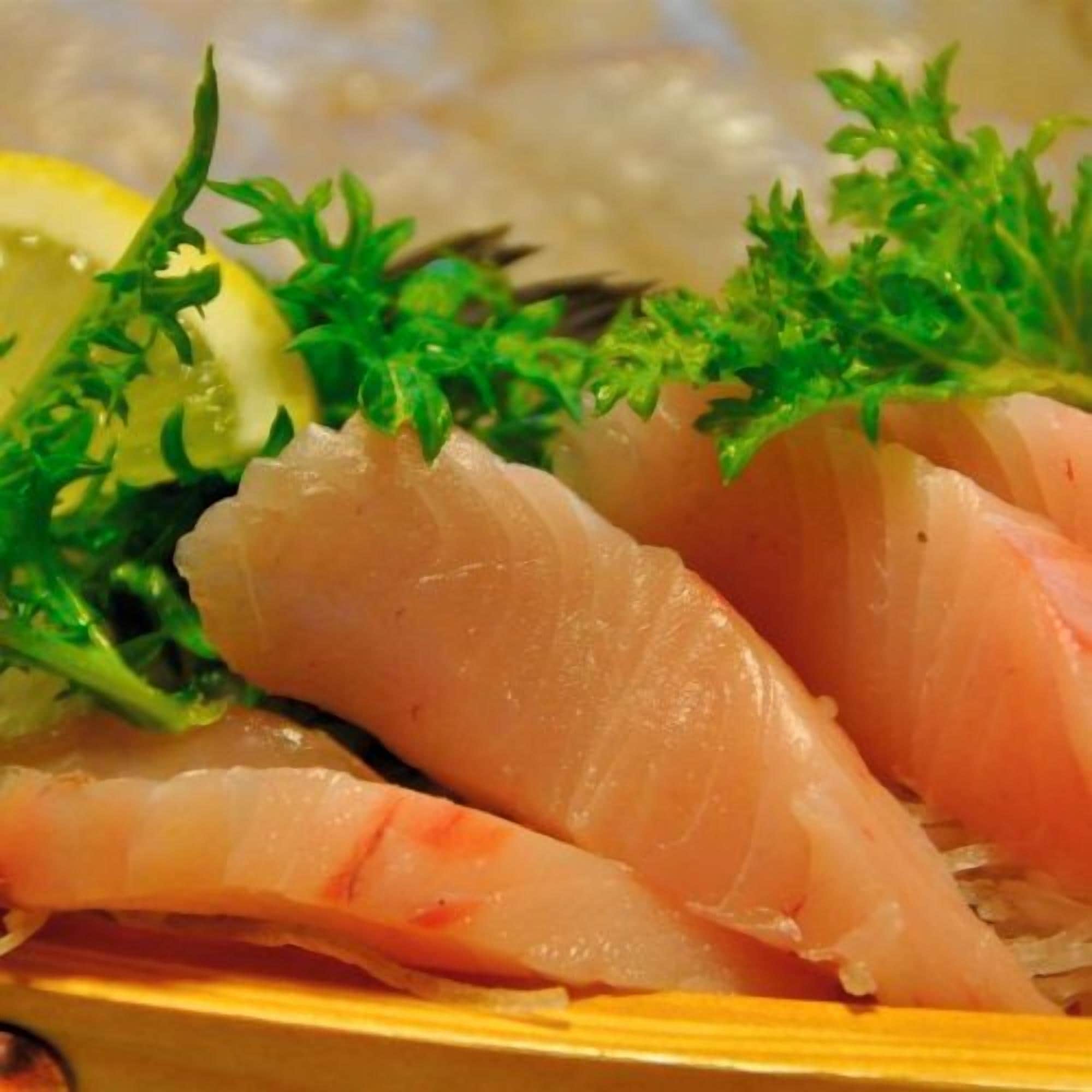 A plate of sashimi with a slice of fish, garnished with parsley and a slice of lemon.