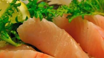 A plate of sashimi with a slice of fish, garnished with parsley and a slice of lemon.