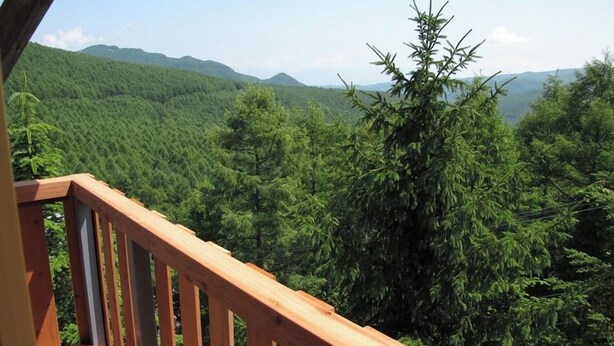 A wooden deck with a view of a forested mountain range. - Hotel Andermatt (Nagawa)