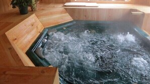 A wooden spa room with a hot tub, wooden flooring, a window with a balcony, and a potted plant. - Hotel Andermatt (Nagawa)