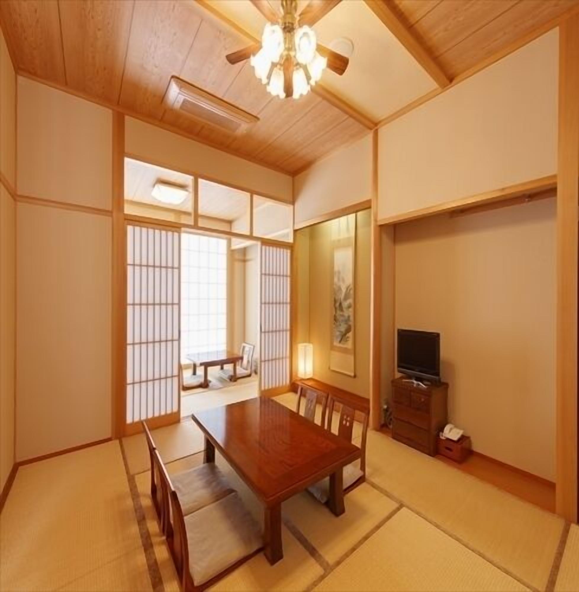 A traditional Japanese-style room with tatami flooring, a wooden dining table, a television, and sliding shoji doors.