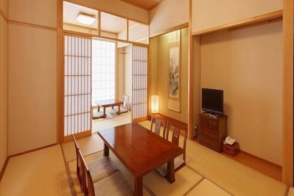 Ein traditioneller japanischer Raum mit Tatami-Bodenbelag, einem Holztisch, einem Fernseher und verschiebbaren Shoji-Türen.