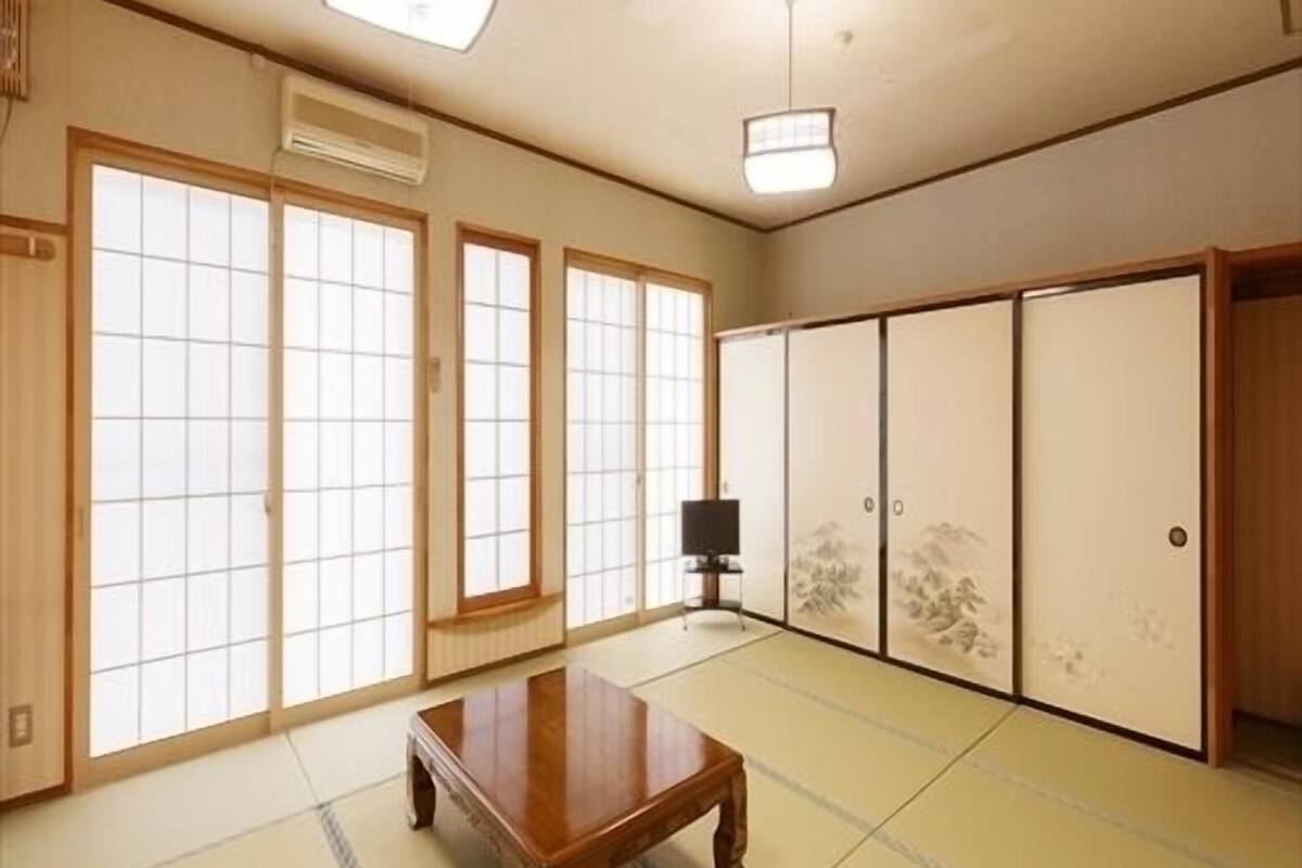 Ein traditioneller japanischer Raum mit Tatami-Bodenbelag, Schiebetüren, einem Fernseher und Deckenventilatoren.