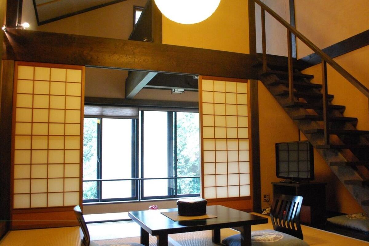 Une pièce de style japonais traditionnel, avec un sol recouvert de tatamis, une table basse, un téléviseur et un escalier.
