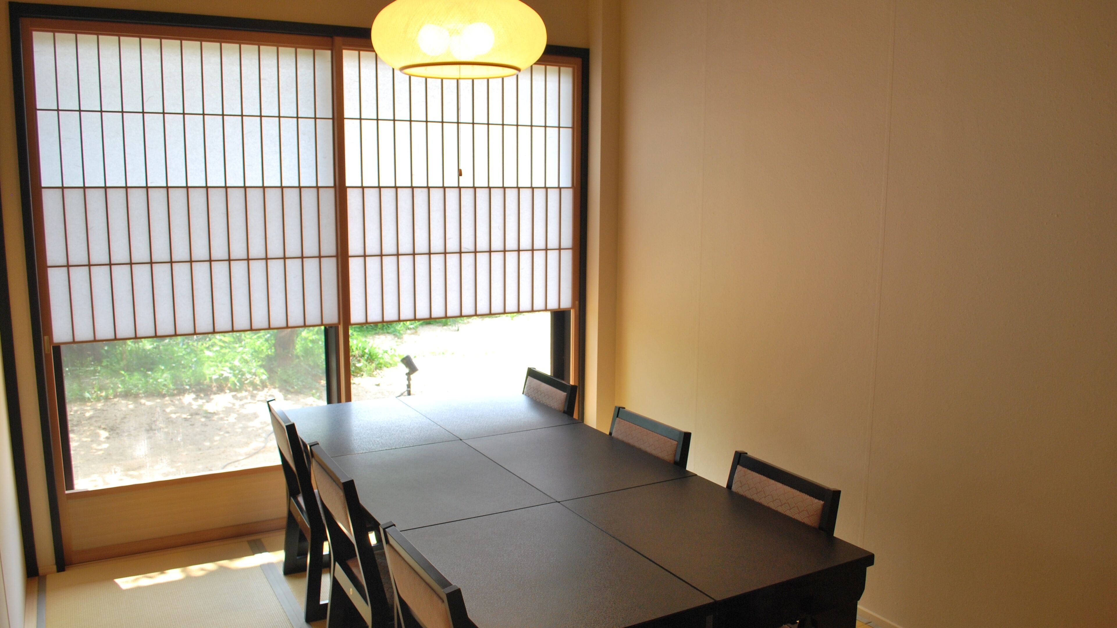 Une pièce avec une table surmontée d’un tatami, une porte coulissante de style japonais traditionnel et un luminaire suspendu.