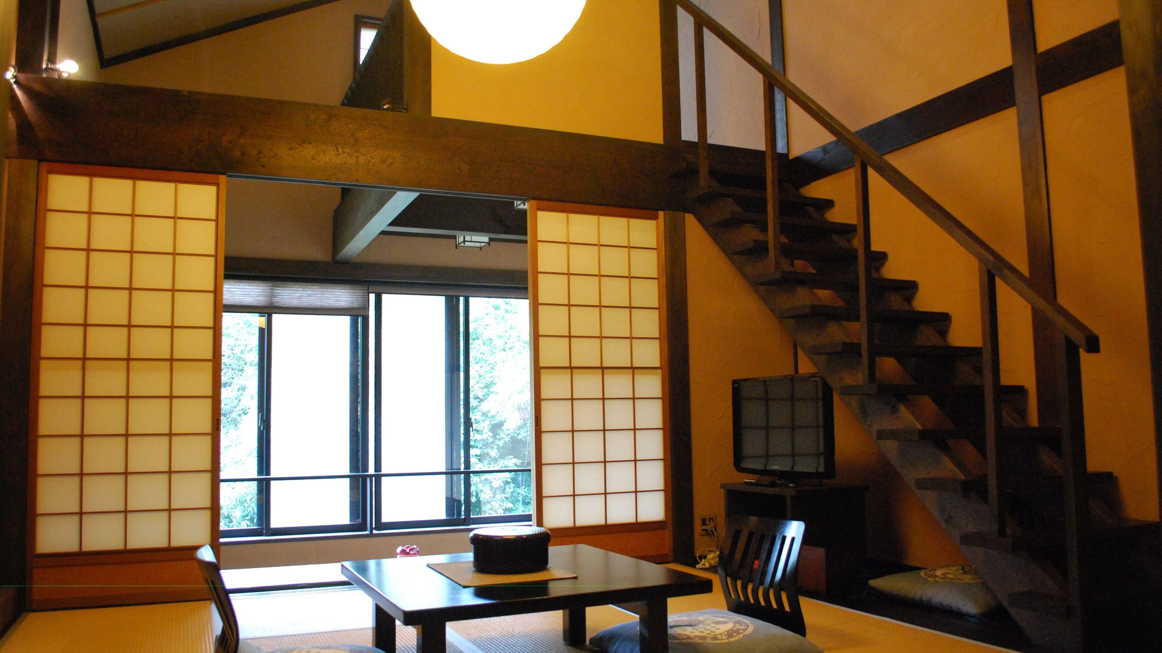 Une pièce de style japonais traditionnel, avec un sol recouvert de tatamis, une table basse, un téléviseur et un escalier en bois.