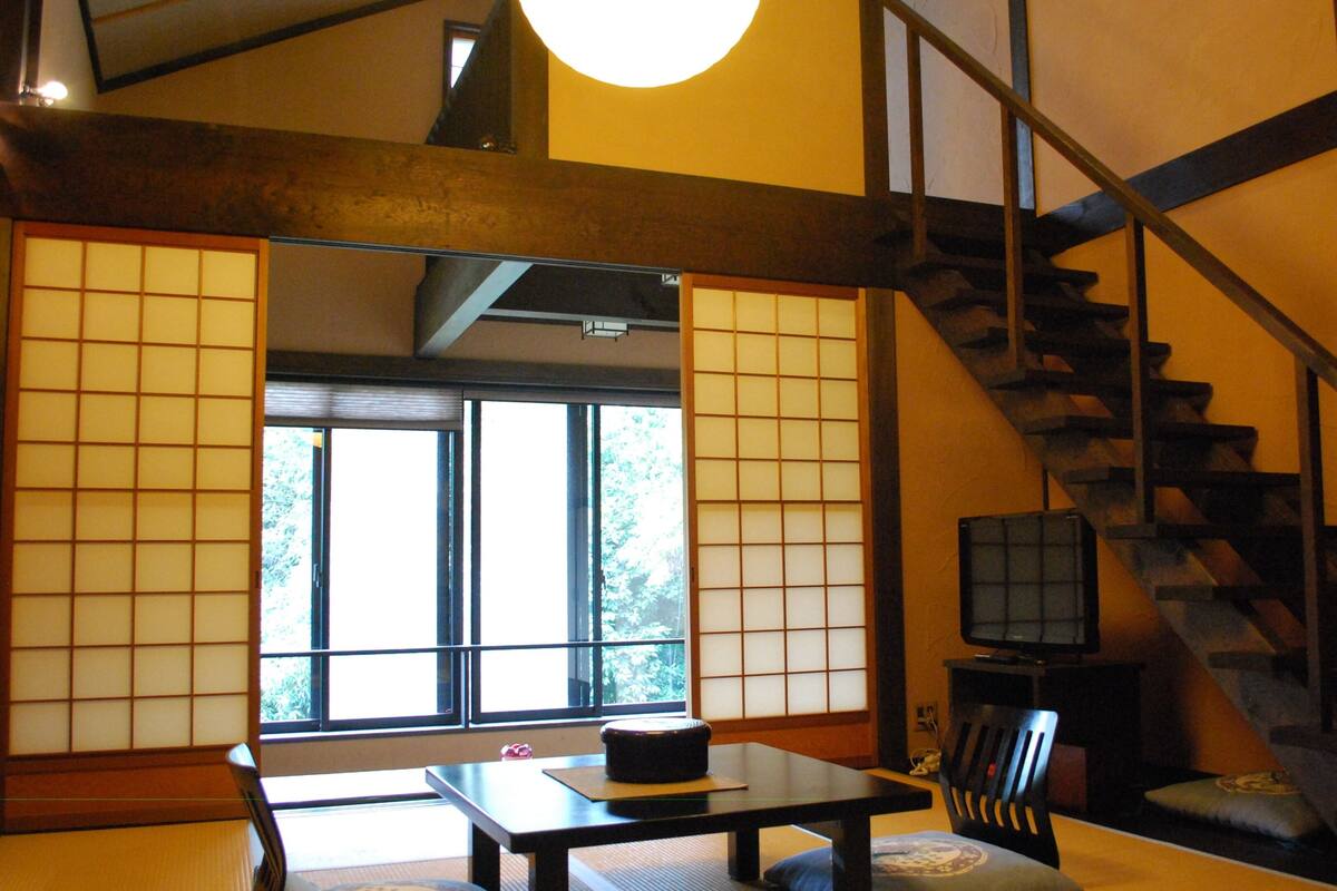 Une pièce de style japonais traditionnel, avec un sol recouvert de tatamis, une table basse, un téléviseur et un escalier en bois.
