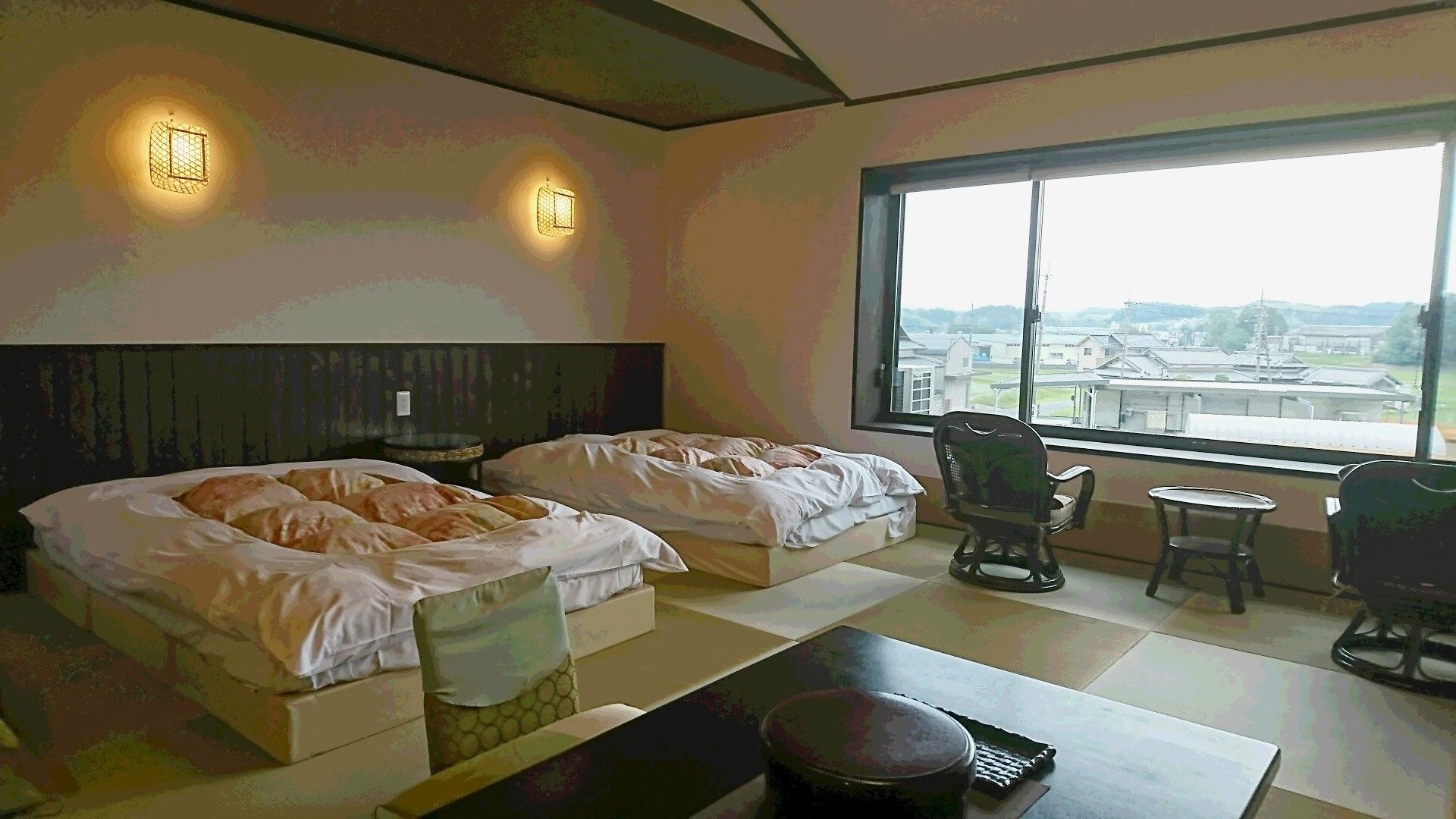 Une chambre d’hôtel avec deux lits, une vue sur la ville et une petite table avec une chaise.