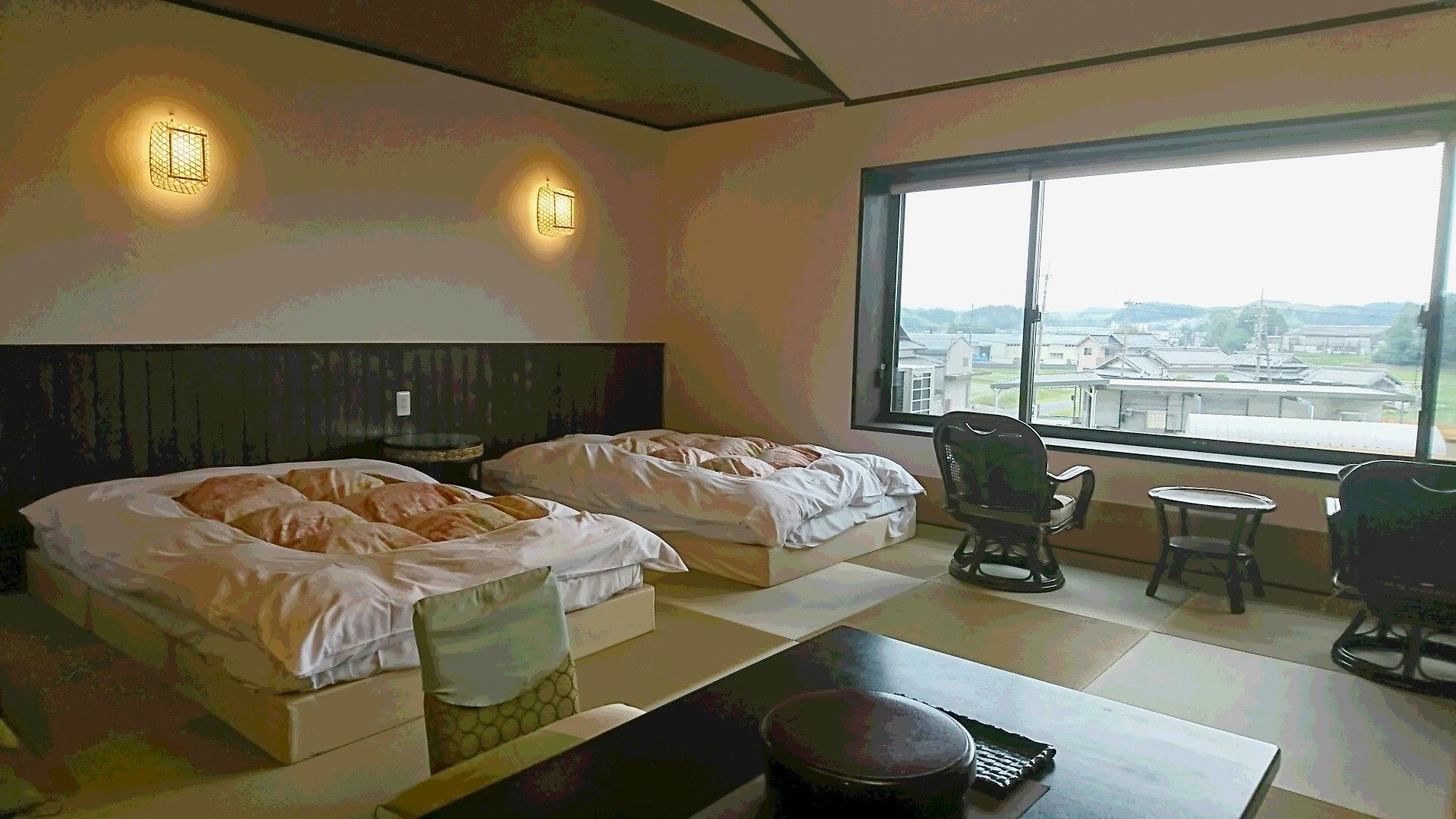 Une chambre d’hôtel avec deux lits, une vue sur la ville et une petite table avec une chaise.
