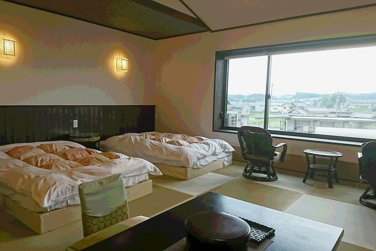 Une chambre d’hôtel avec deux lits, une vue sur la ville et une petite table avec une chaise.