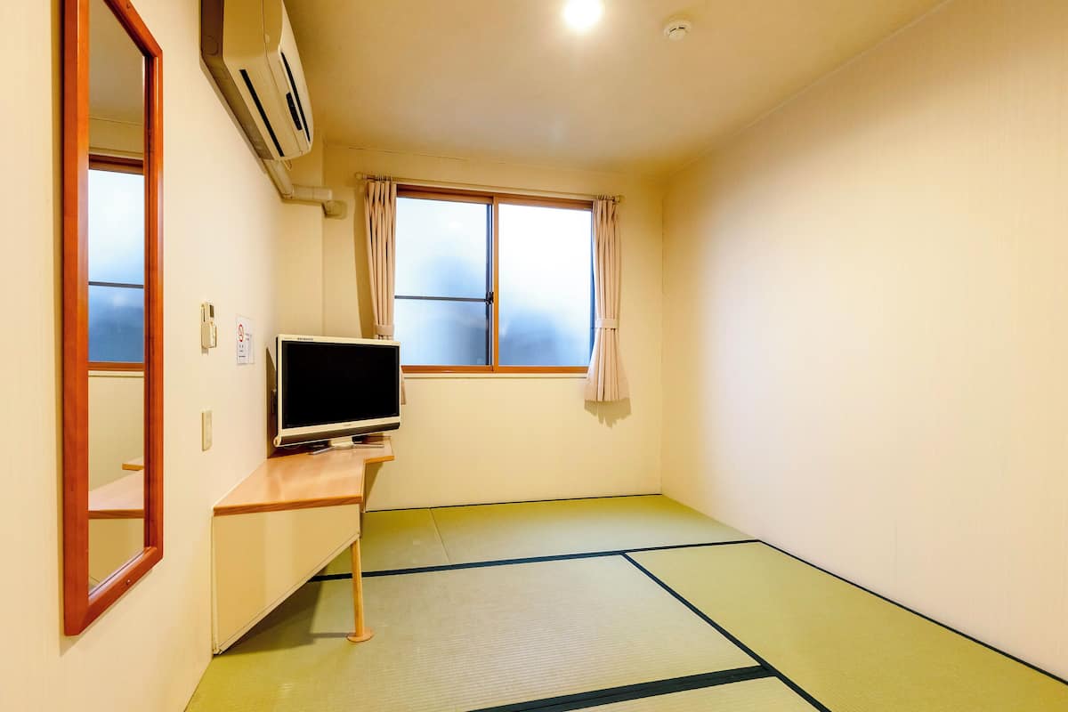 A room with tatami flooring, a television on a stand, a sliding door, and a window with curtains.