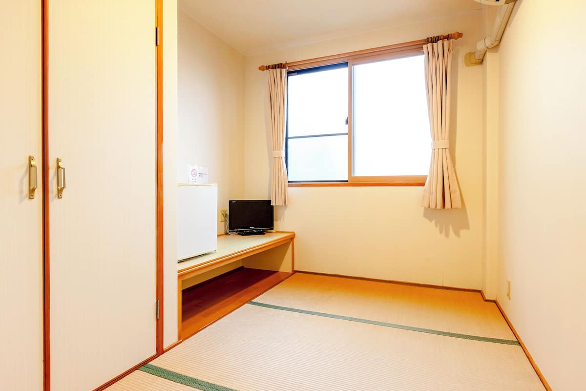 A room with tatami flooring, a desk with a computer, a window with curtains, and a door.