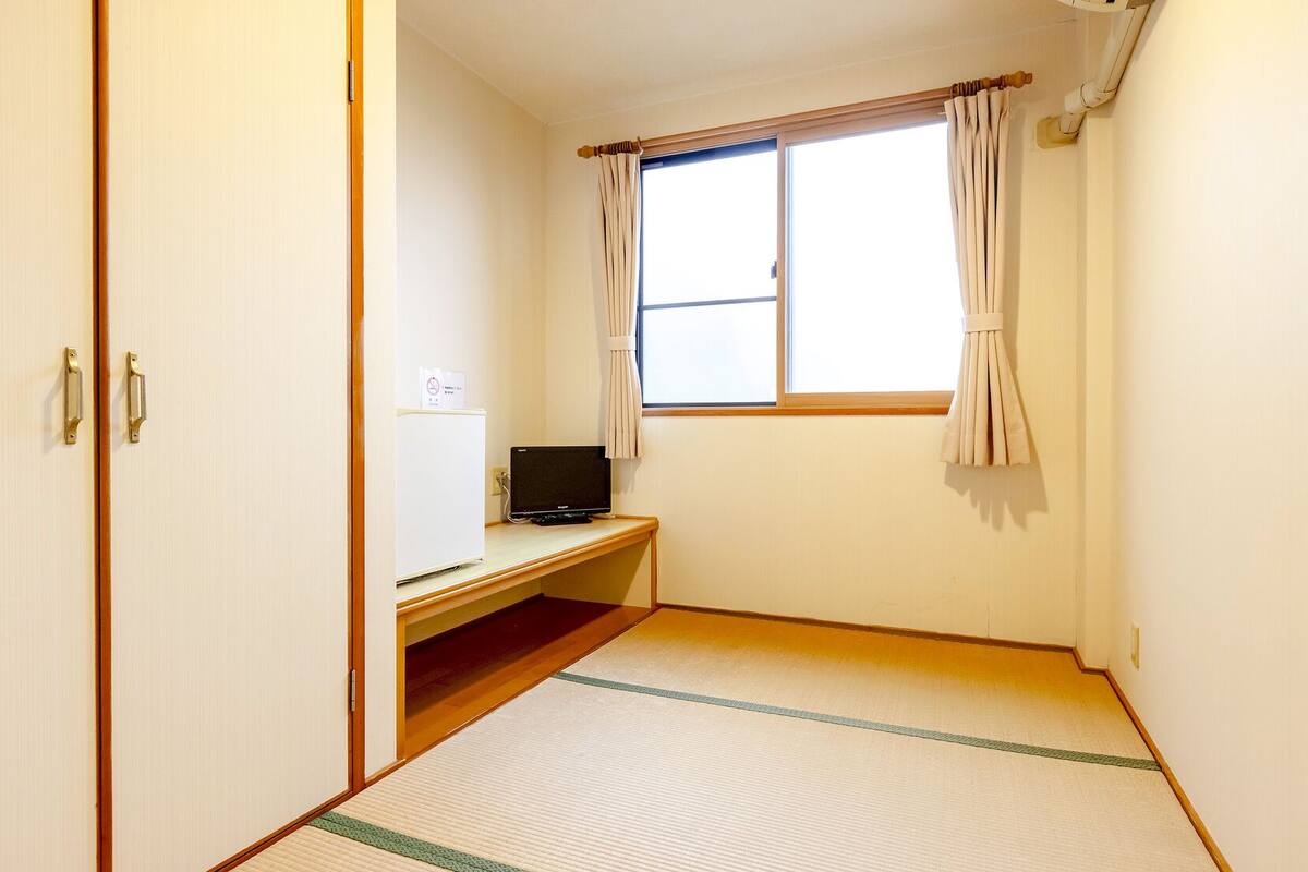 A room with tatami flooring, a desk with a laptop, a window with curtains, and a wardrobe.