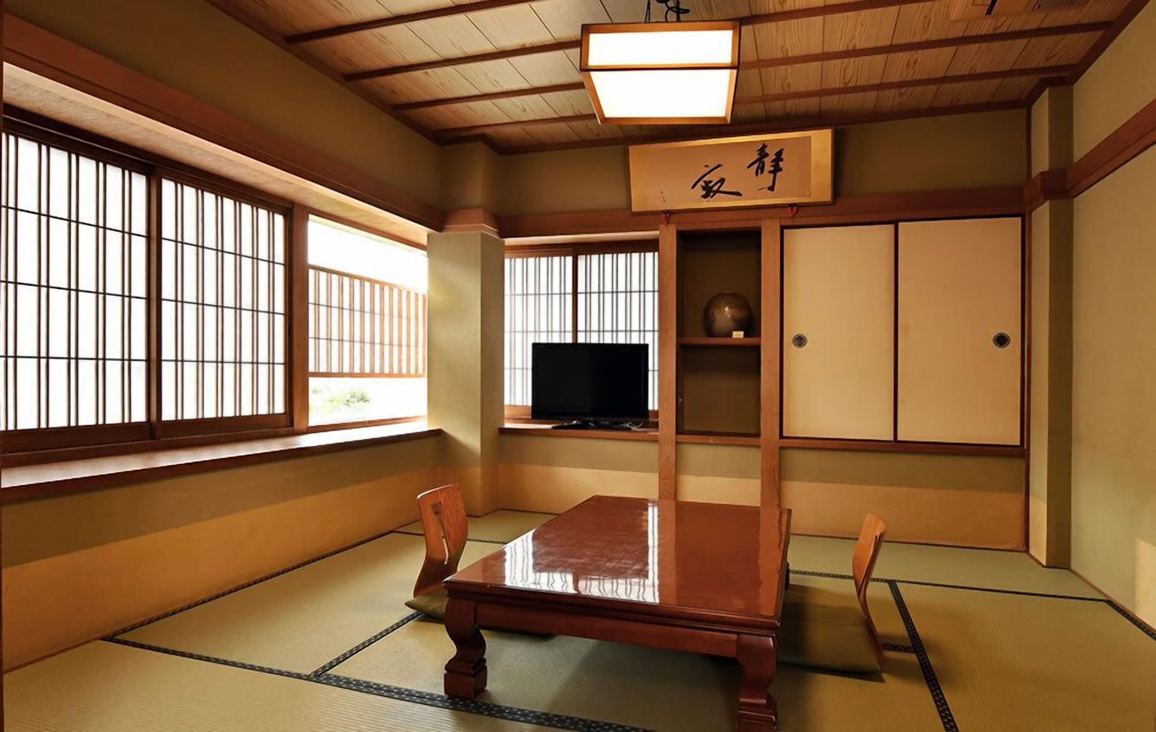 Ein traditioneller japanischer Raum mit Tatami-Boden, einem niedrigen Holztisch, einem Fernseher, Schiebetüren und einem Schild mit japanischen Schriftzeichen.