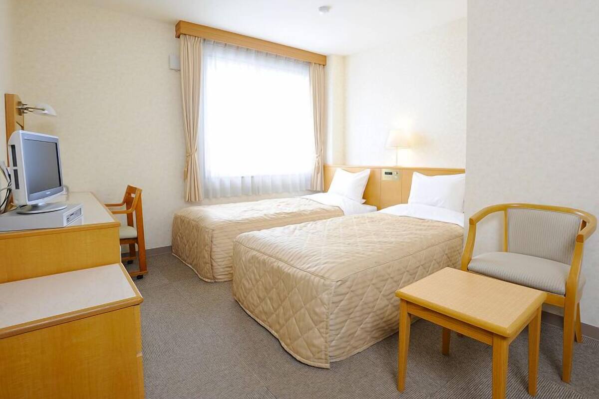 Une chambre d’hôtel avec deux lits, un bureau avec un ordinateur, une chaise et une lampe.