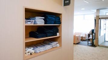 A hotel room with a wooden shelf displaying folded towels and linens.