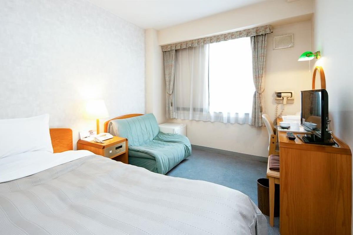 Habitación de hotel con dos camas, un escritorio con ordenador, una silla y una ventana con cortinas.