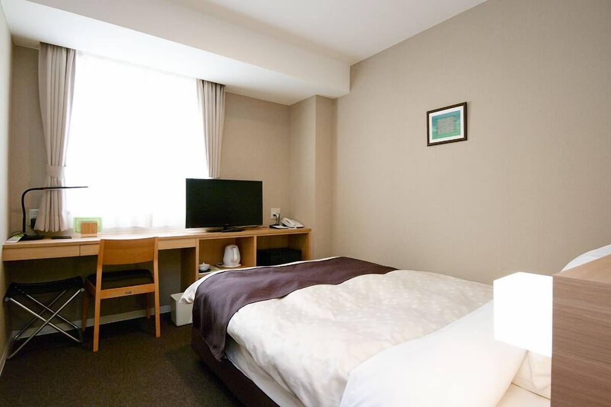 Une chambre d’hôtel avec un lit, un bureau équipé d’un ordinateur, une télévision et un petit tableau accroché au mur.