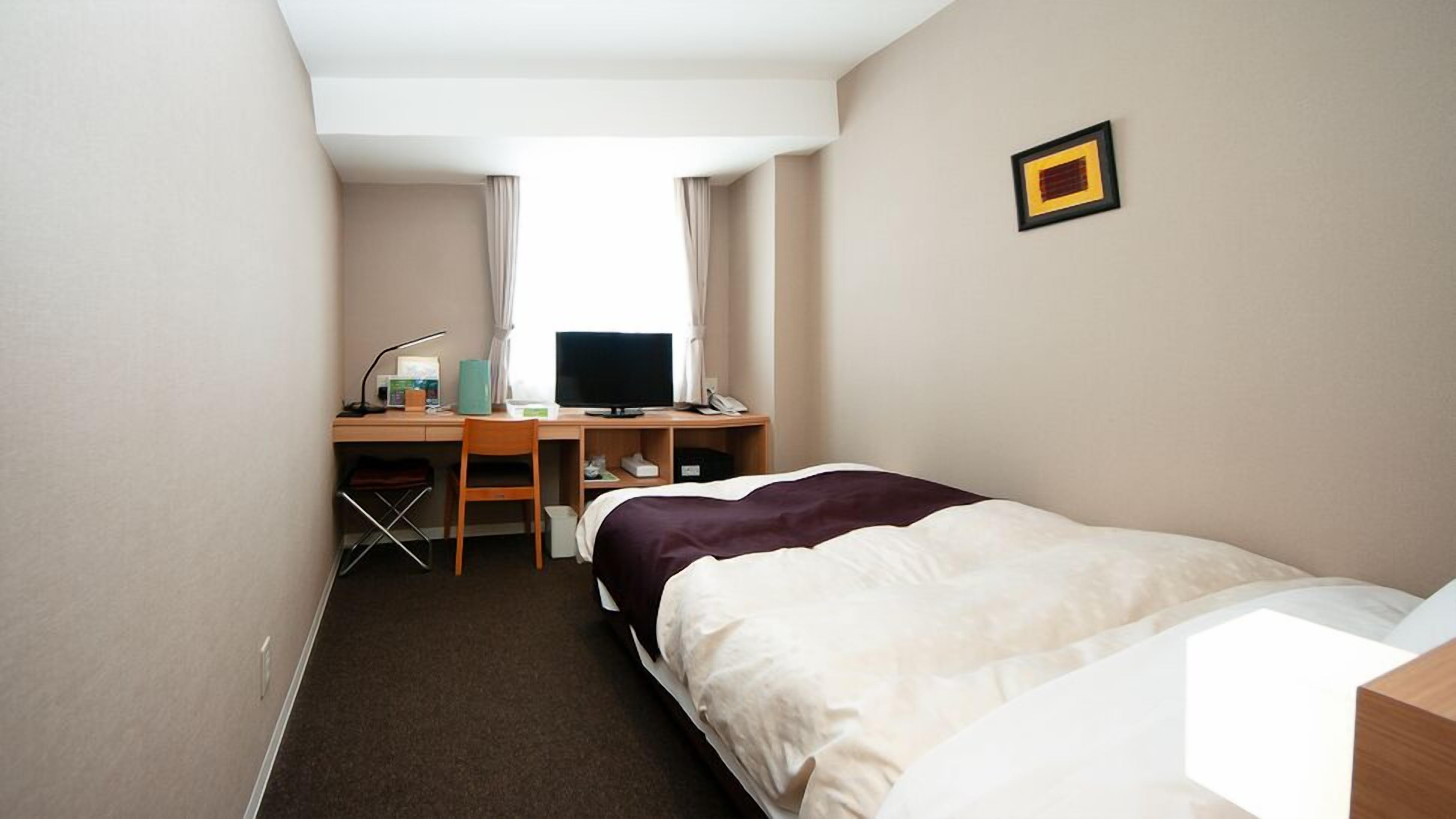 A hotel room with a bed, a desk with a computer, a chair, and a small table.