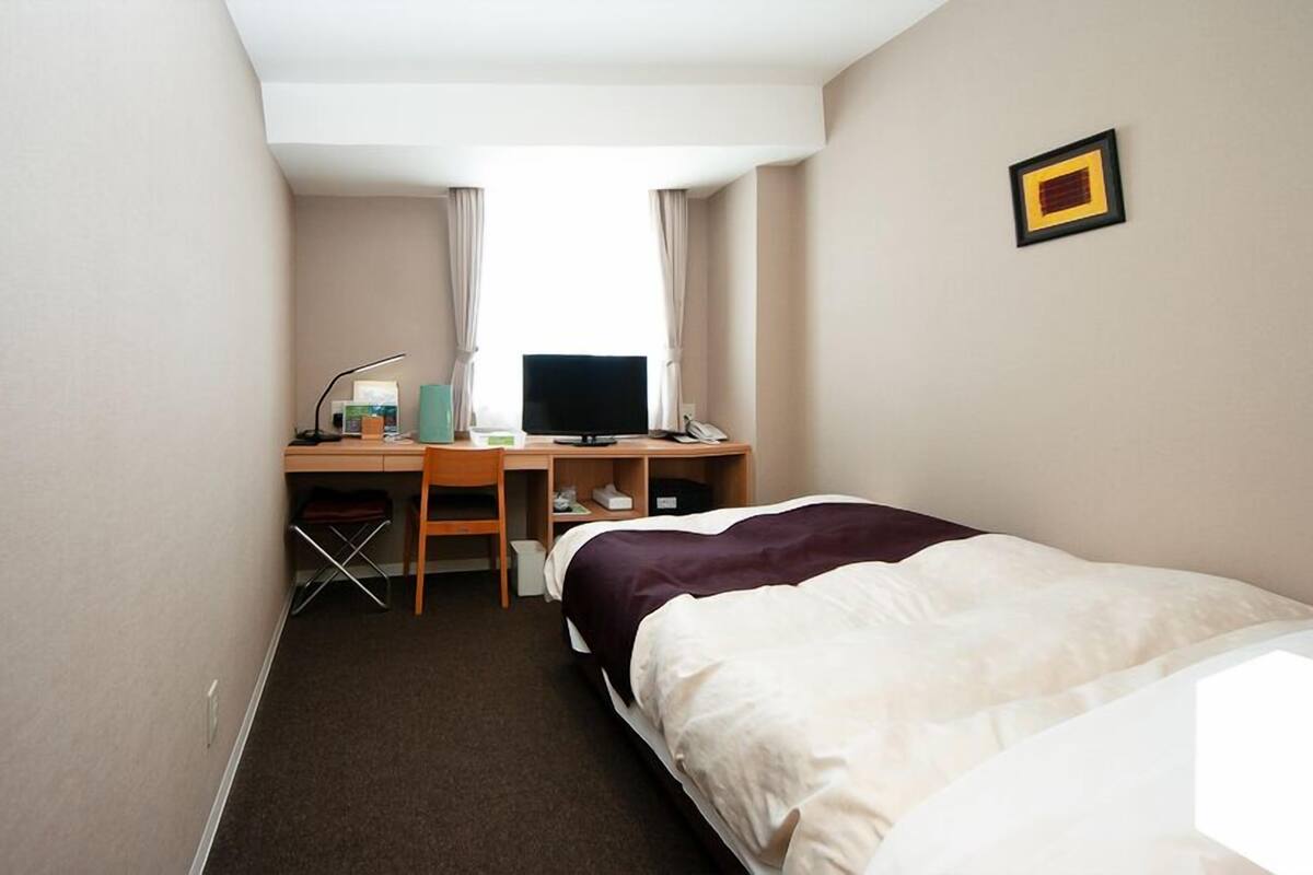 Une chambre d’hôtel avec un lit, un bureau avec un ordinateur, une chaise et une petite table.