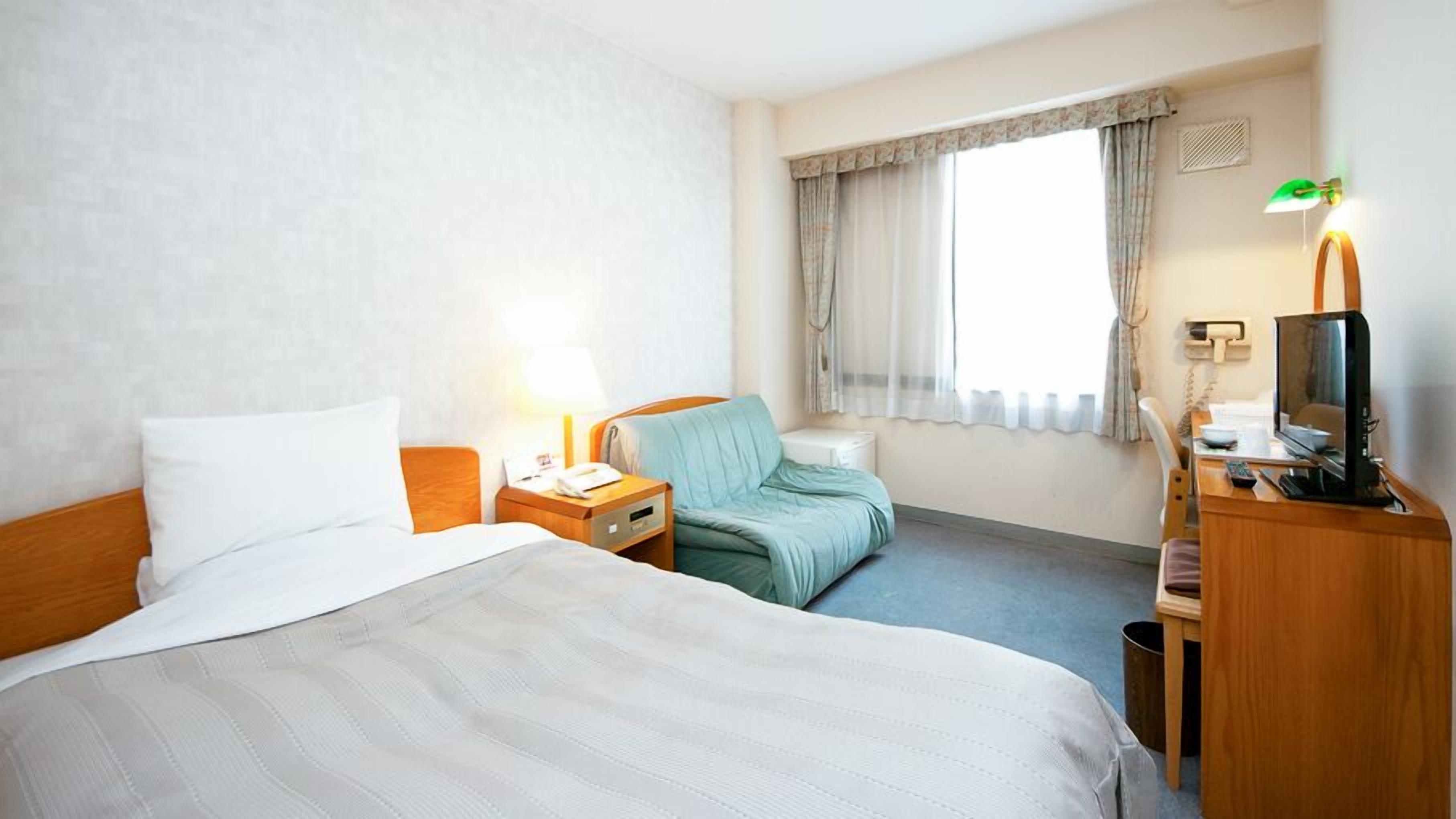 A hotel room with two beds, a desk with a computer, a chair, and a window with curtains.