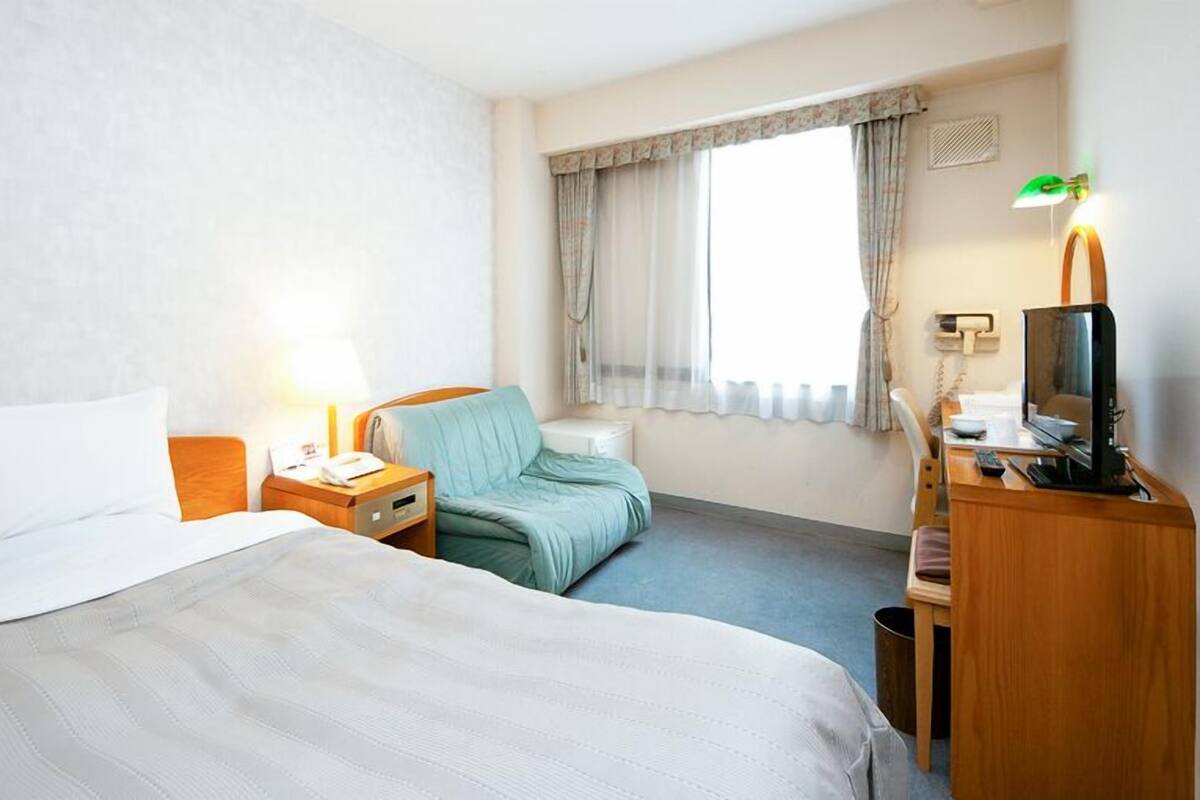 Une chambre d’hôtel avec deux lits, un bureau avec un ordinateur, une chaise et une fenêtre avec des rideaux.