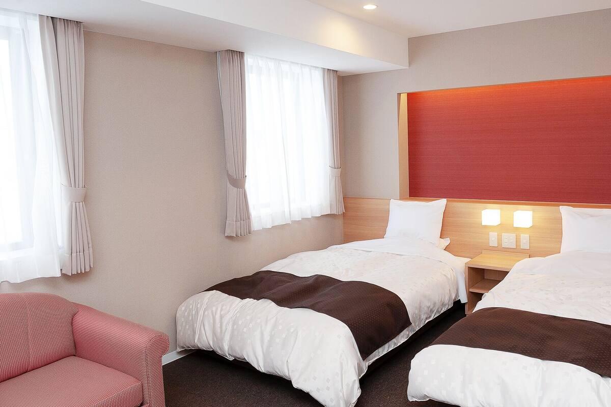 Une chambre d’hôtel avec deux lits, un mur d’accent rouge, une table de chevet avec des lampes et un canapé rouge.