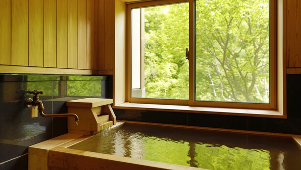 A wooden interior with a large window, a wooden bathtub, and a faucet.