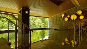 A spa pool with a wooden staircase, stone walls, and a view of trees.