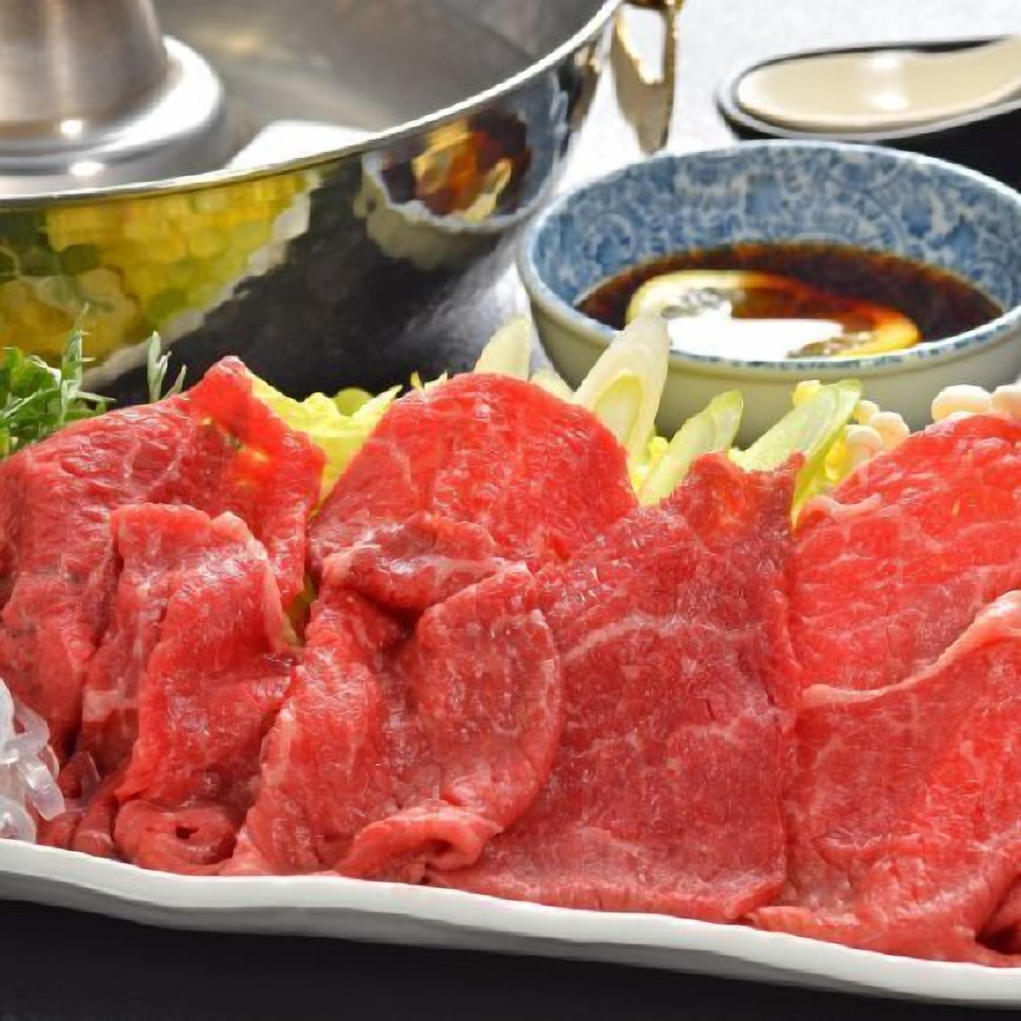 A plate of raw beef slices, a bowl of dipping sauce, and a pot on a table.