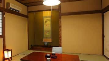 A traditional Japanese room with tatami flooring, a low table, and a hanging light fixture.