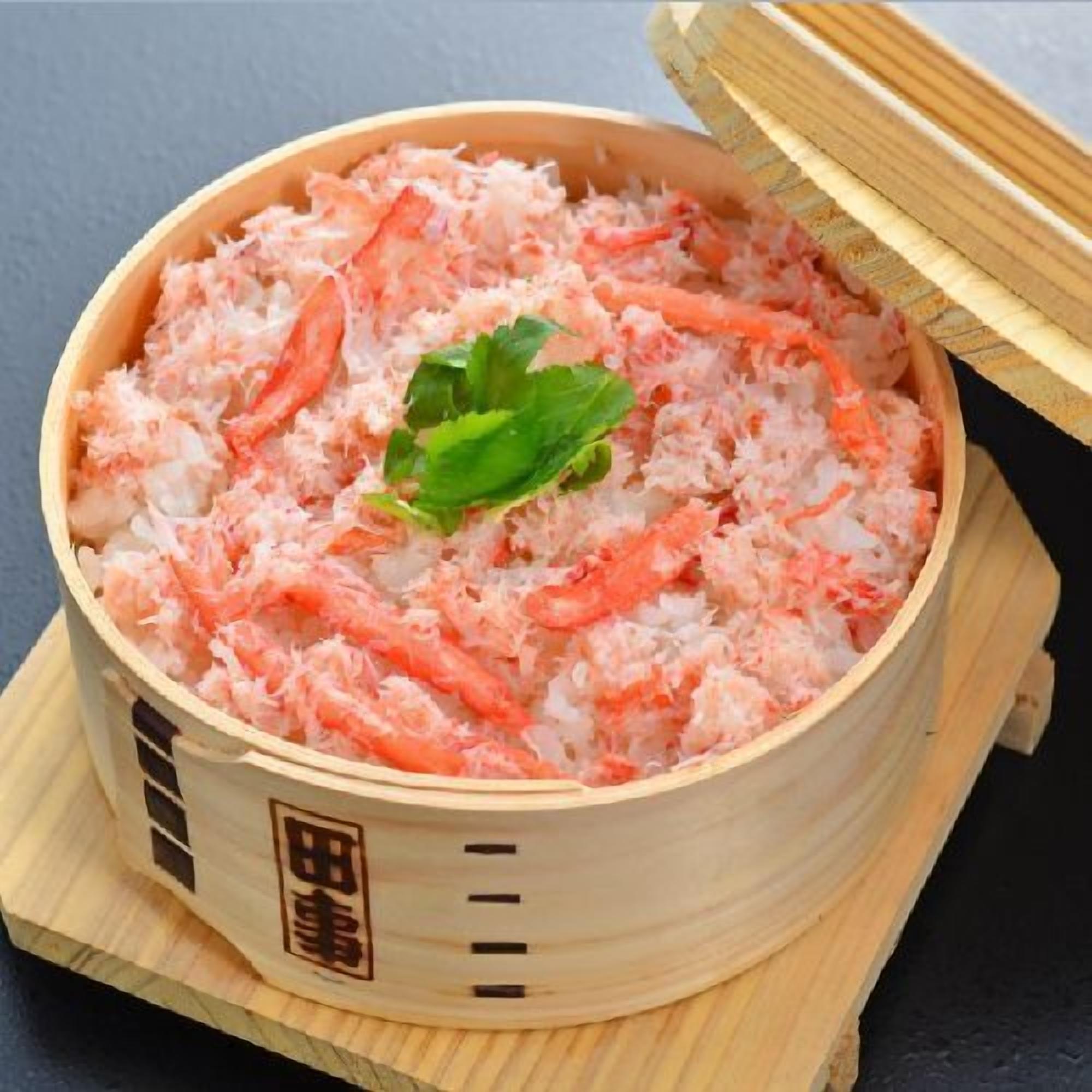 A wooden container with a lid, filled with a pinkish food item, possibly a type of seafood or vegetable dish, garnished with a green leaf.