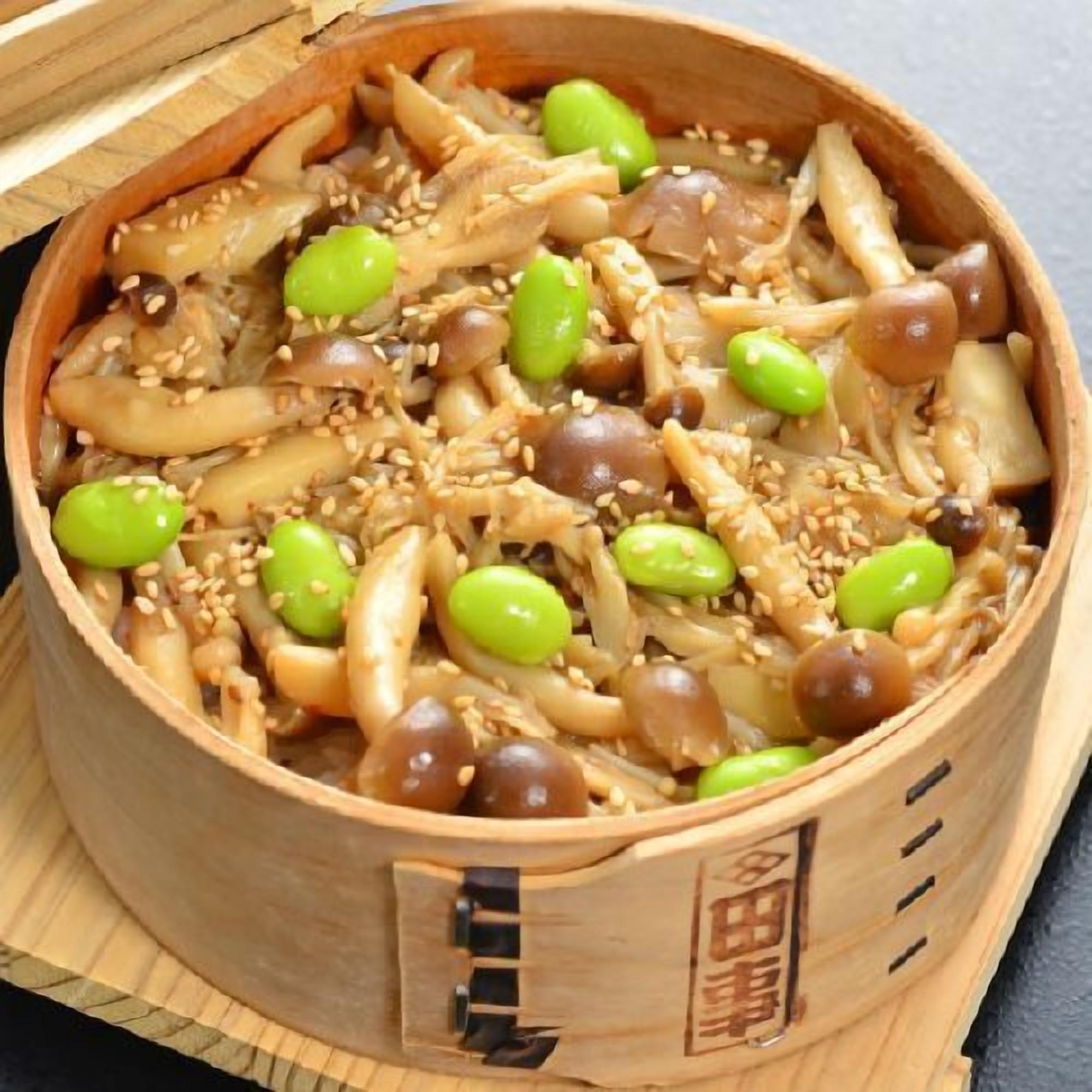 A wooden container filled with a dish of noodles, edamame, and sesame seeds.