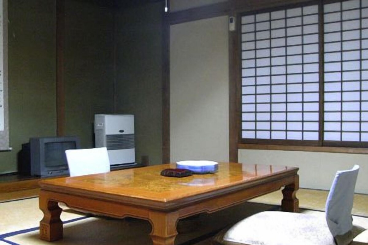 Una habitación japonesa tradicional con suelo de tatami, una mesa de madera, un televisor y un panel de shoji.